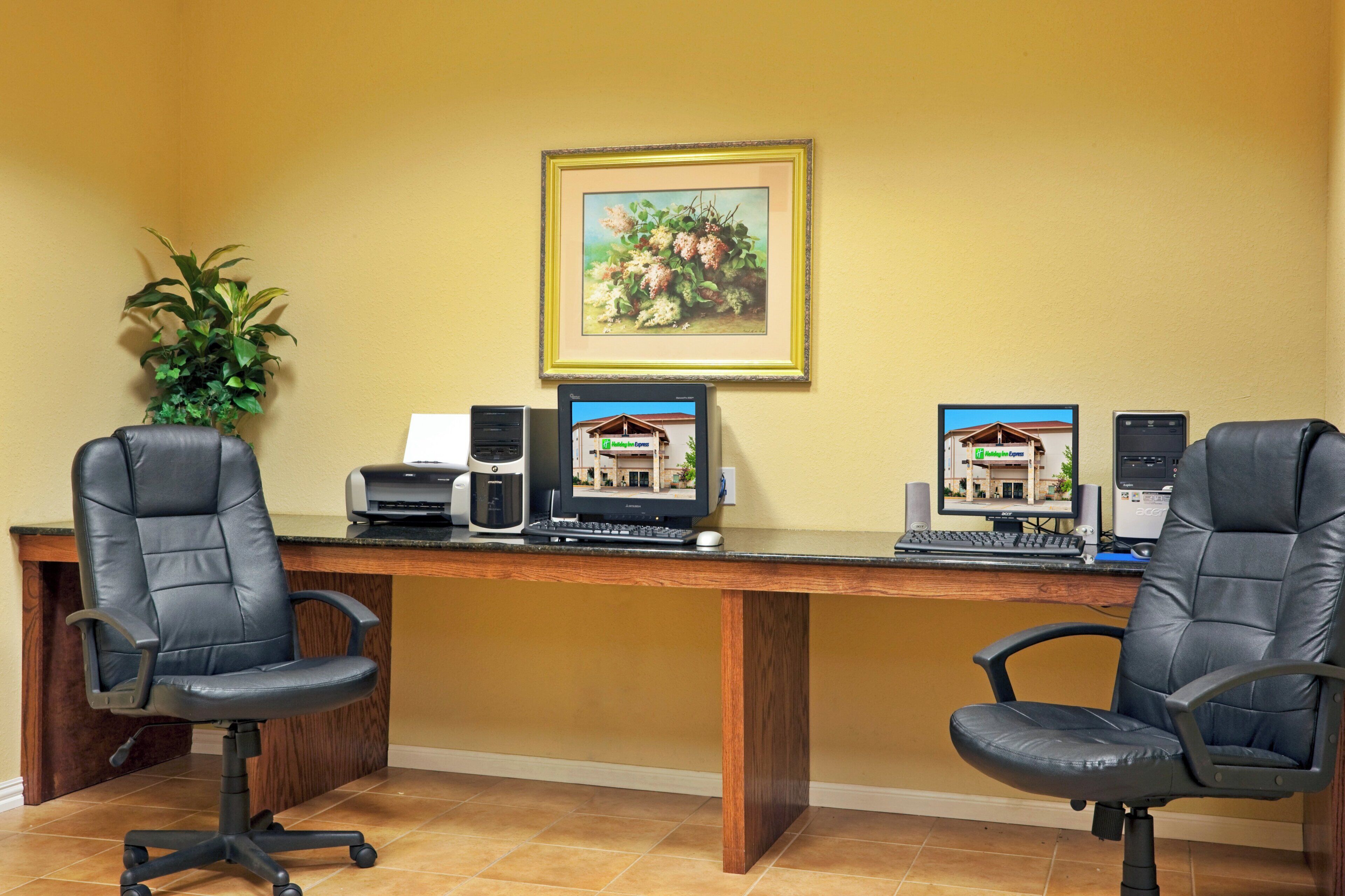 A hotel reception desk with two black leather chairs, a desktop computer, a printer, and a framed picture on the wall.