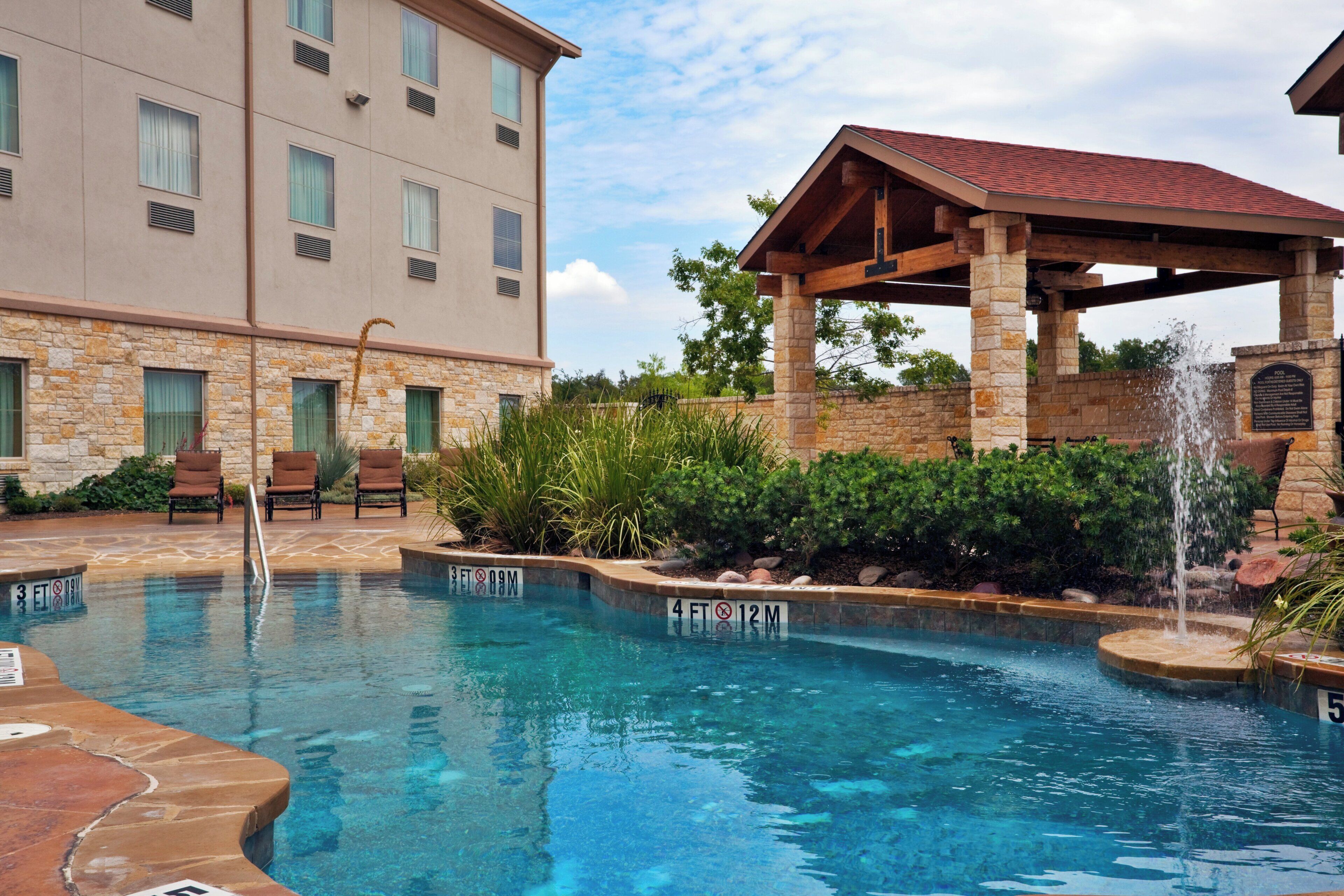A hotel pool area with a stone building, lounge chairs, and a covered seating area.
