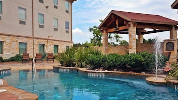 A hotel pool area with a stone building, lounge chairs, and a covered seating area.