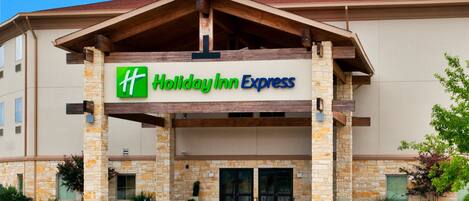 A Holiday Inn Express building with a stone facade, a covered entrance, and a clear blue sky.