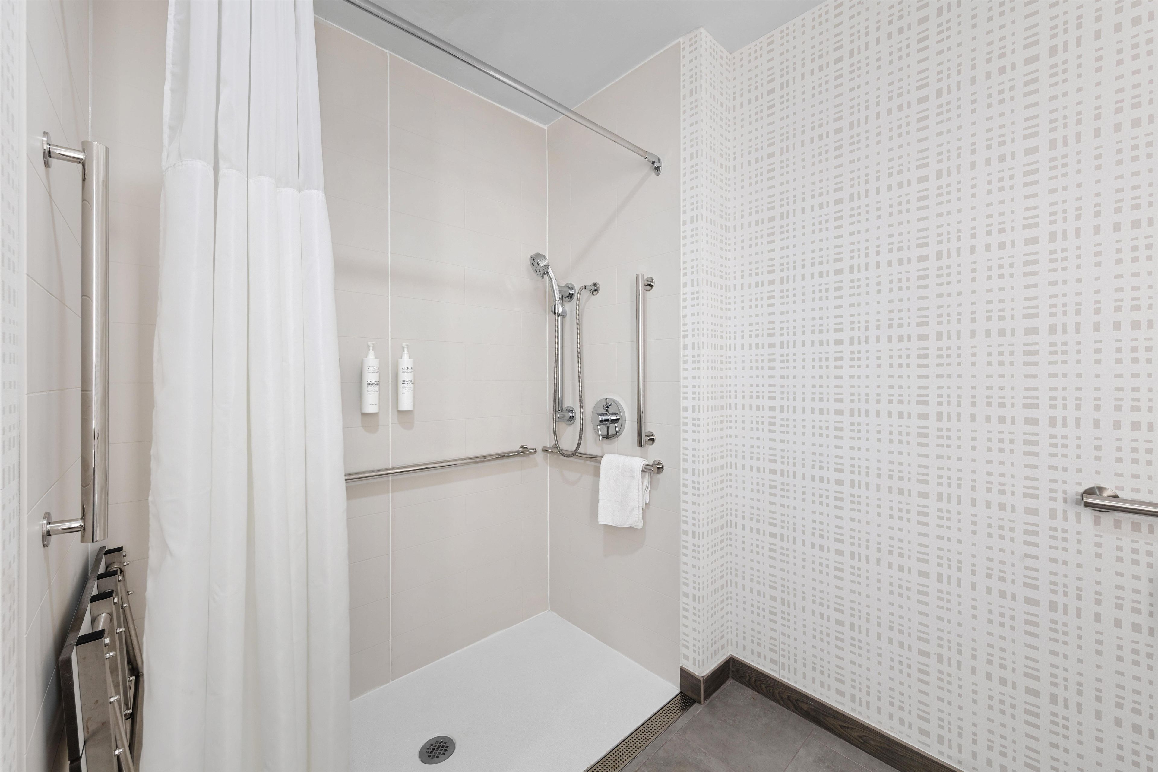A modern shower area with a glass door, a handheld showerhead, a handheld showerhead, and a towel rack.