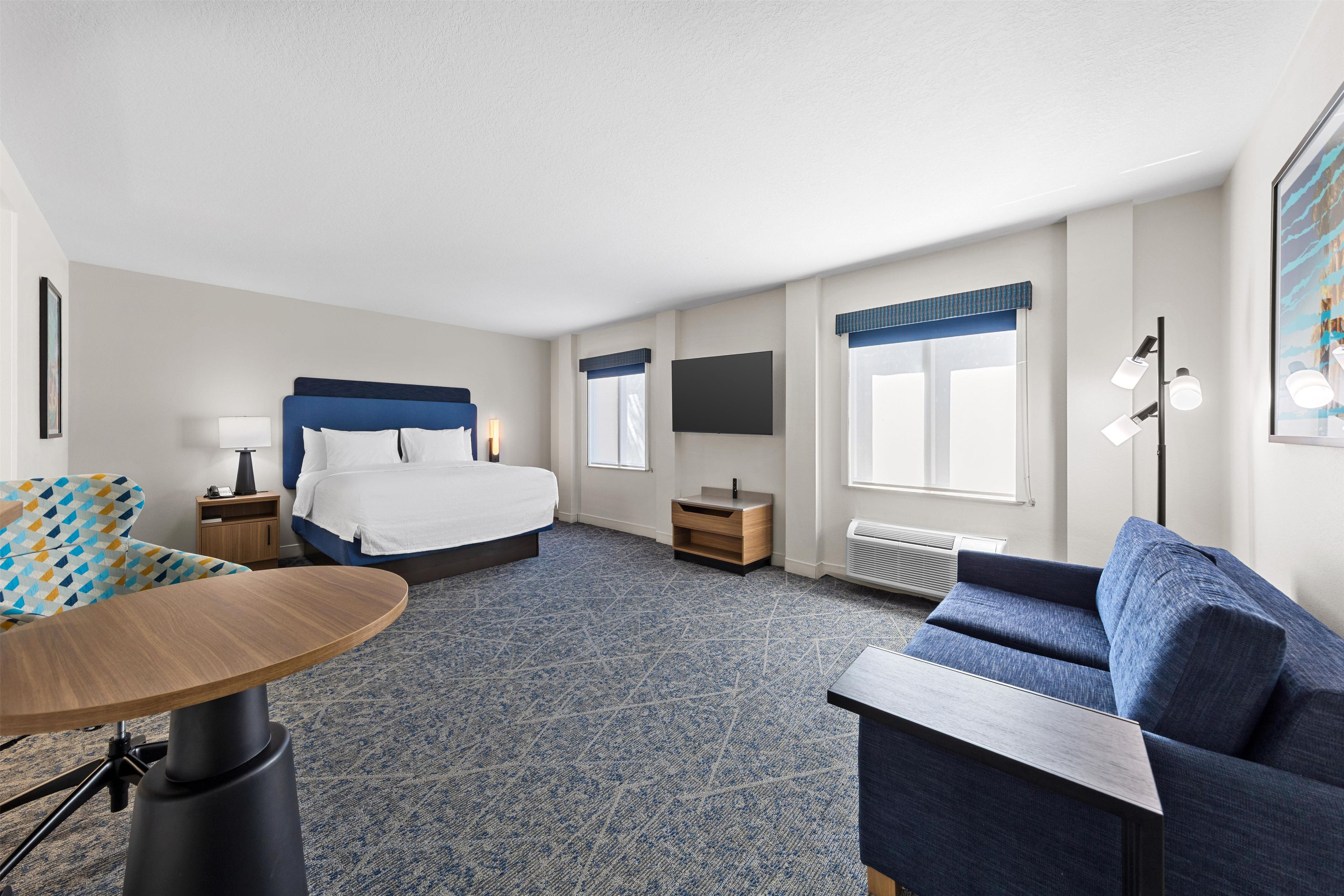 A hotel room with a bed, a desk, a chair, a sofa, a TV, and a window with curtains.