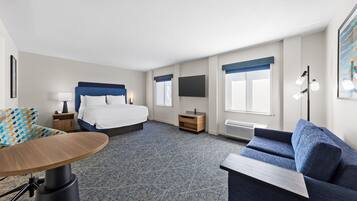 A hotel room with a bed, a desk, a chair, a sofa, a TV, and a window with curtains.