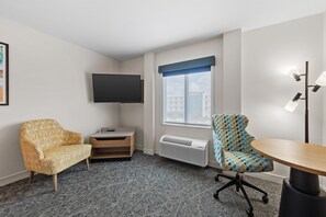 A hotel room with a flat-screen TV, a sofa, a patterned armchair, a small table, and a floor lamp.