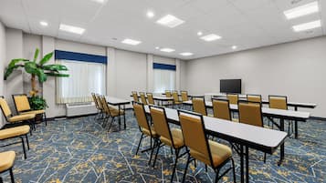 A conference room with tables and chairs, a large plant, and a flat-screen TV.