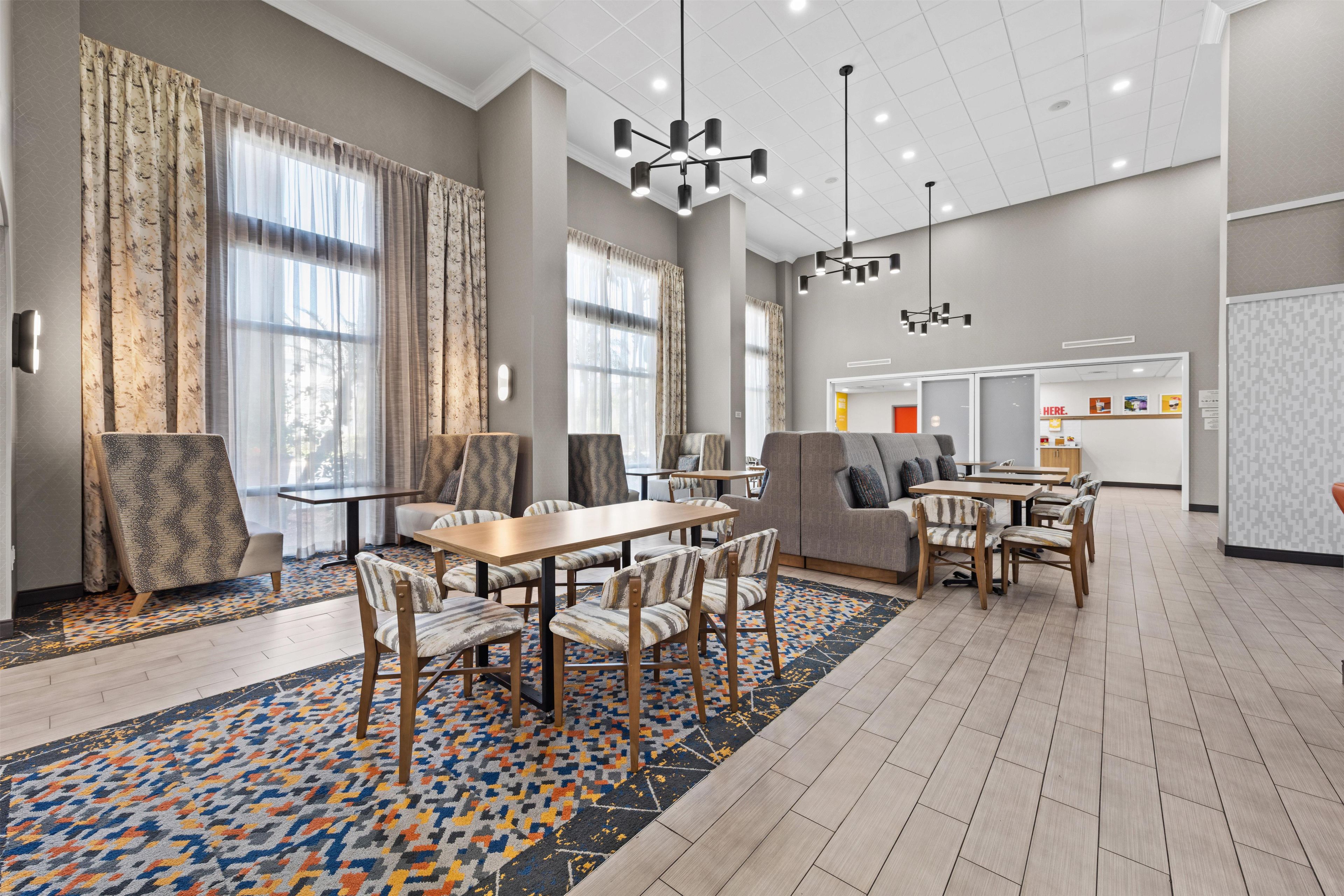 A spacious hotel lobby with a dining area, large windows, and modern lighting fixtures.