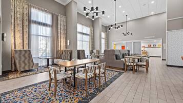 A spacious hotel lobby with a dining area, large windows, and modern lighting fixtures.