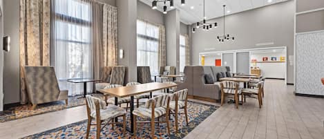 A spacious hotel lobby with a dining area, large windows, and modern lighting fixtures.