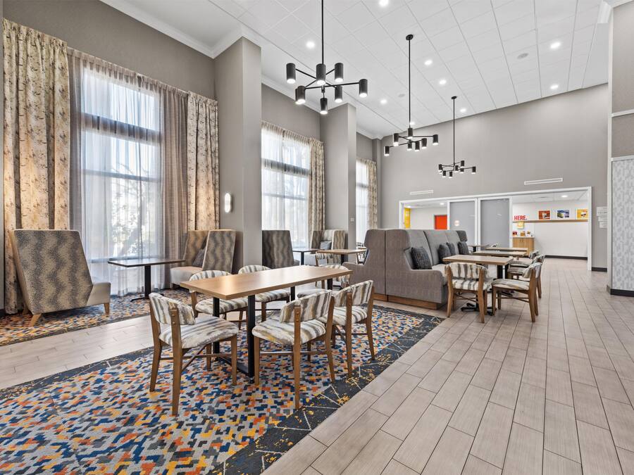 Un amplio vestíbulo de hotel con zona de comedor, ventanas grandes y luminarias modernas.