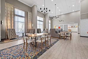A spacious hotel lobby with a dining area, large windows, and modern lighting fixtures.