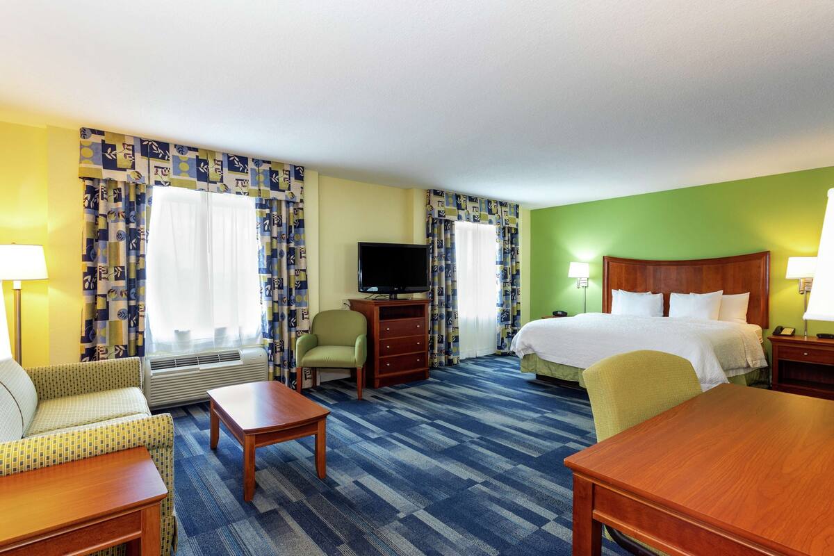 Une chambre d’hôtel avec un lit, deux chaises, une télévision, un bureau et une lampe.