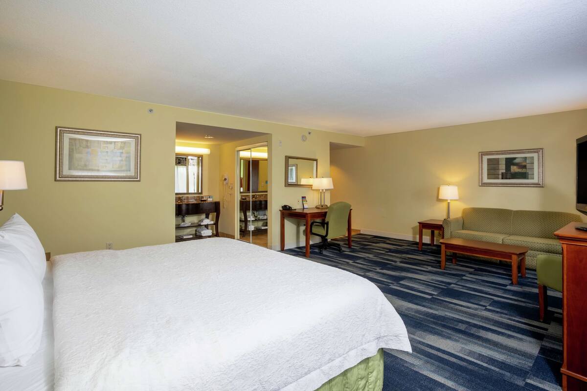 Une chambre d’hôtel avec un grand lit, un bureau, une chaise, un canapé et un sol recouvert de moquette.