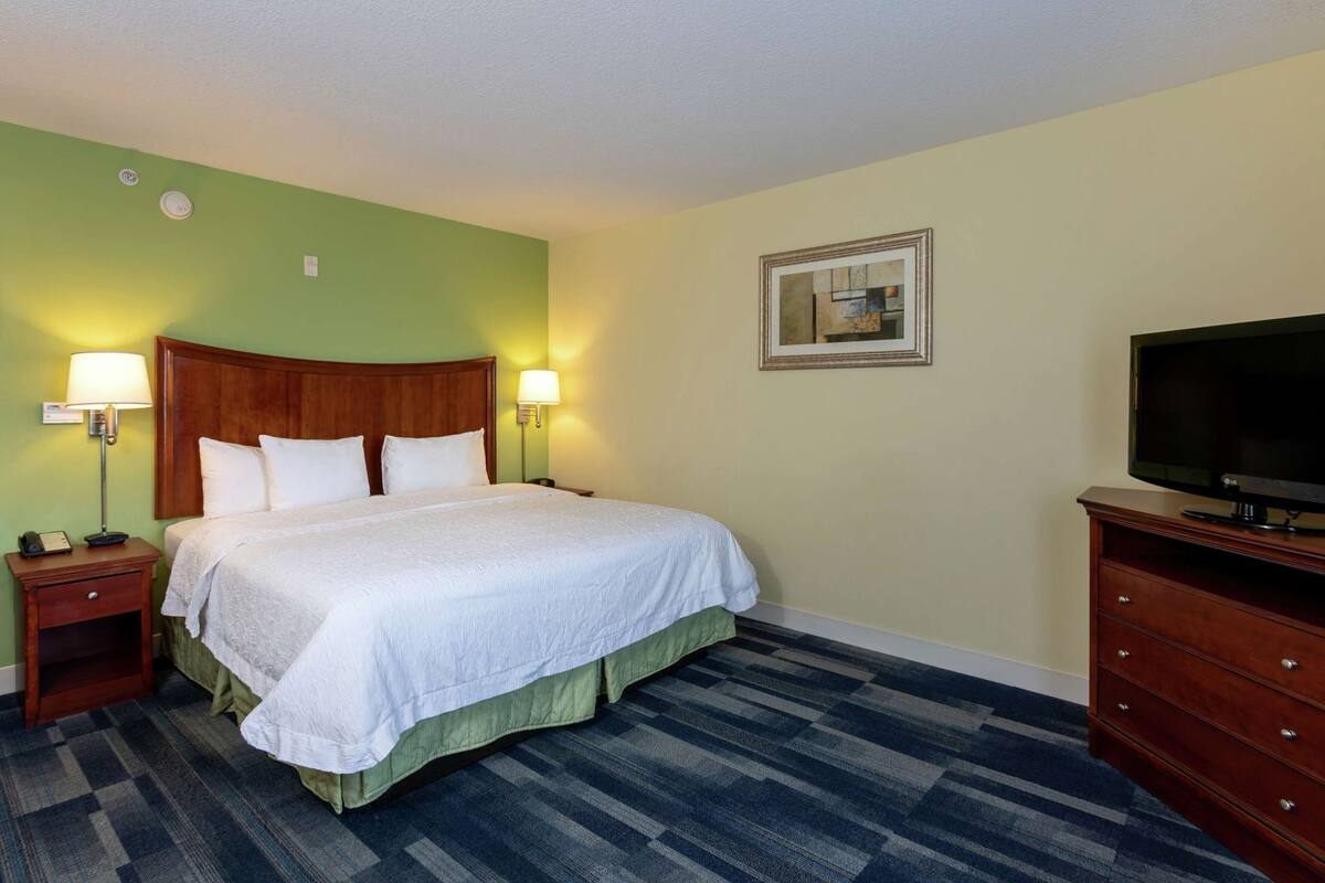 A hotel room with a large bed, two bedside lamps, a television, a dresser, and a framed picture on the wall.