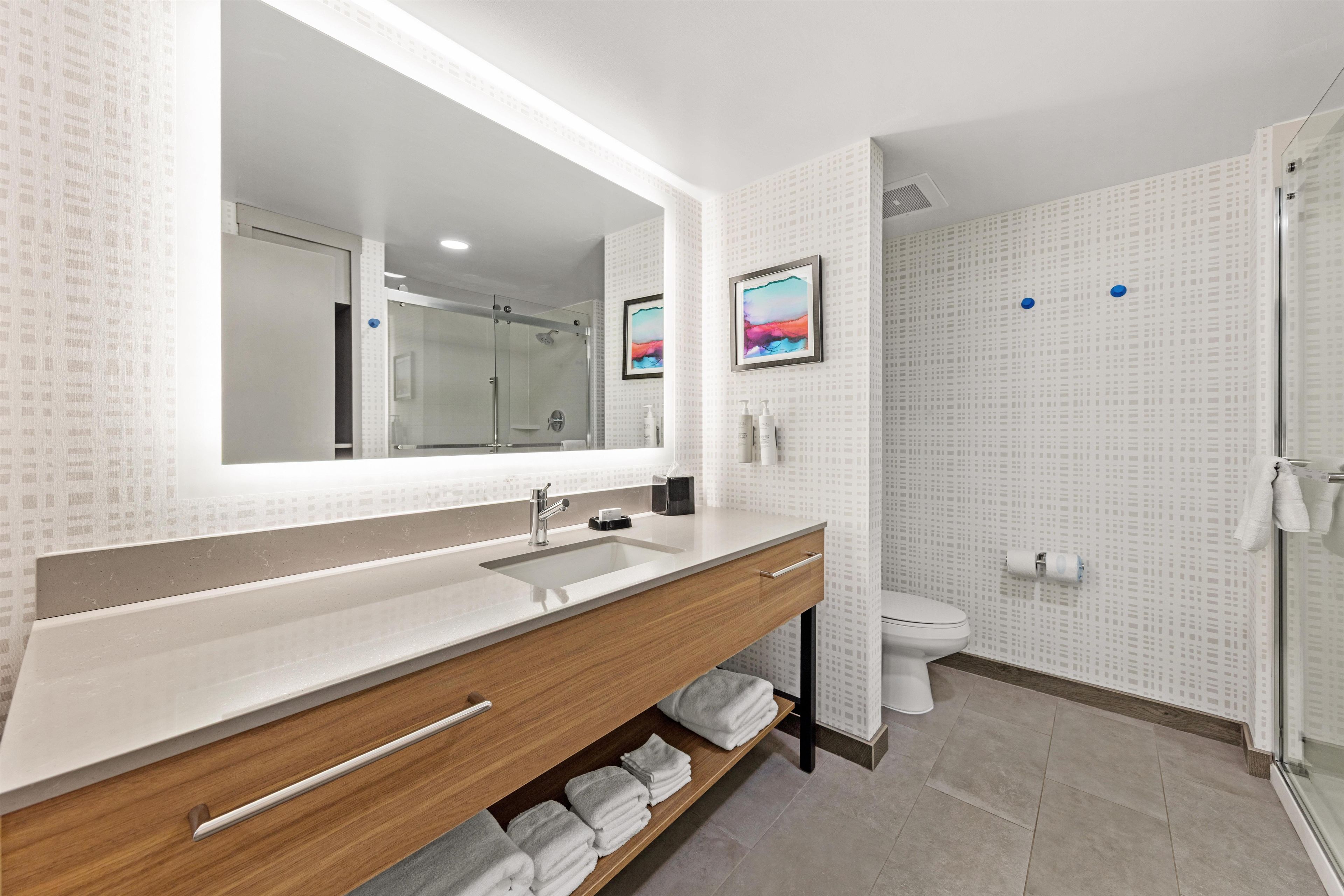 A modern bathroom with a large mirror, a sink, a toilet, and a shower area.