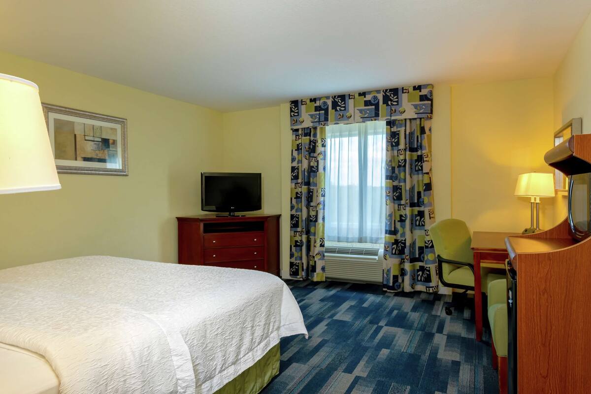 Une chambre d’hôtel équipée d’un lit, d’un bureau, d’une chaise, d’une télévision et d’une fenêtre avec des rideaux.