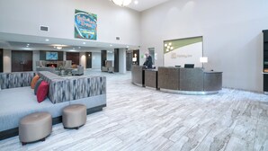 A hotel lobby with a reception desk, seating area, and a large artwork on the wall. - Holiday Inn Atlanta/Roswell by IHG (Roswell)