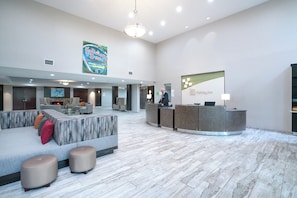 A hotel lobby with a reception desk, seating area, and a large artwork on the wall.
