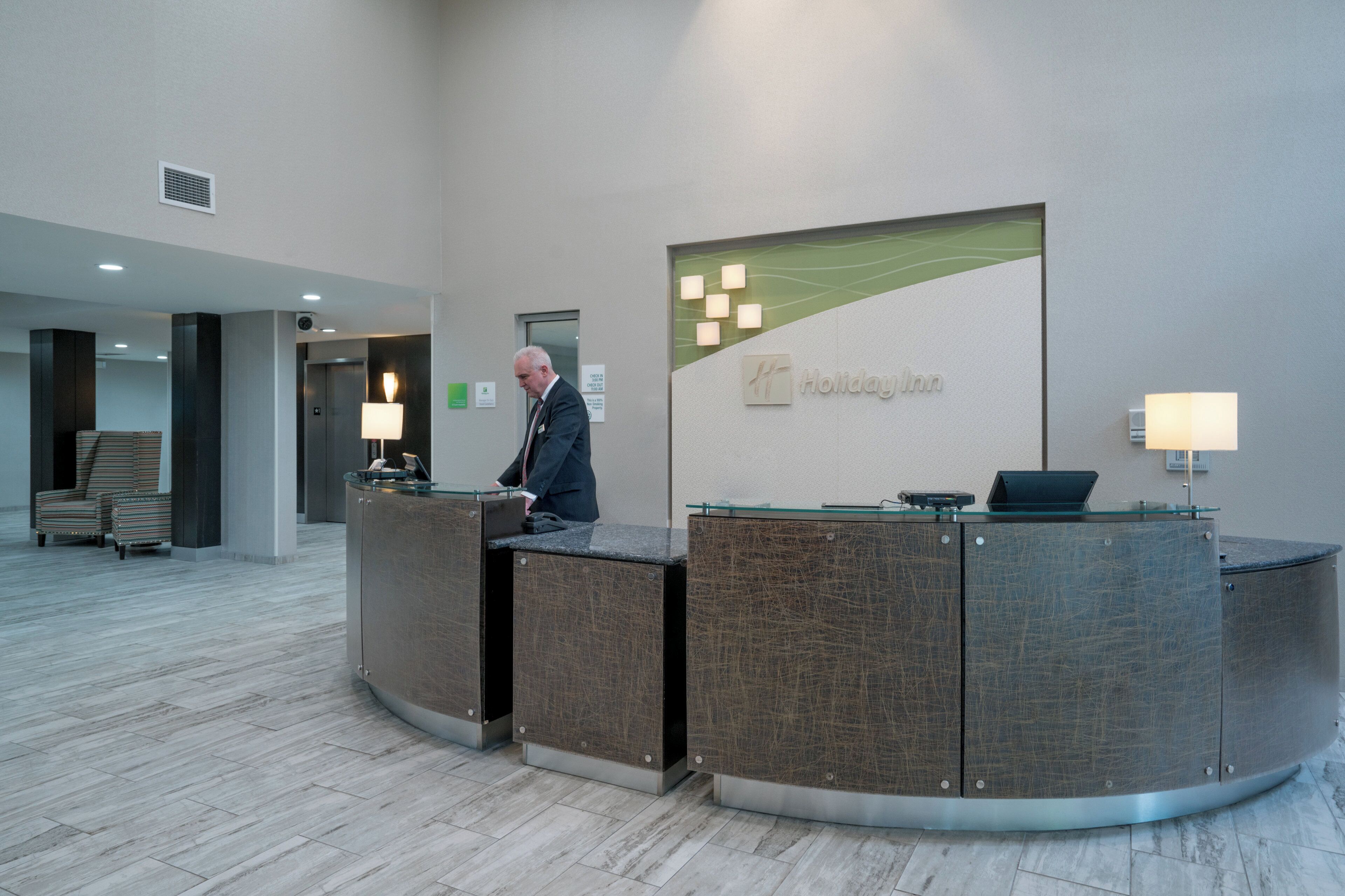 A hotel reception desk with a glass top and a sign for Holiday Inn. There are two lamps on either side of the desk, and a man is standing behind it.