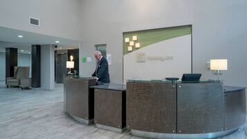 A hotel reception desk with a glass top and a sign for Holiday Inn. There are two lamps on either side of the desk, and a man is standing behind it.