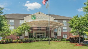A Holiday Inn hotel with a covered entrance, American flag, and landscaped surroundings. - Holiday Inn Atlanta/Roswell by IHG (Roswell)