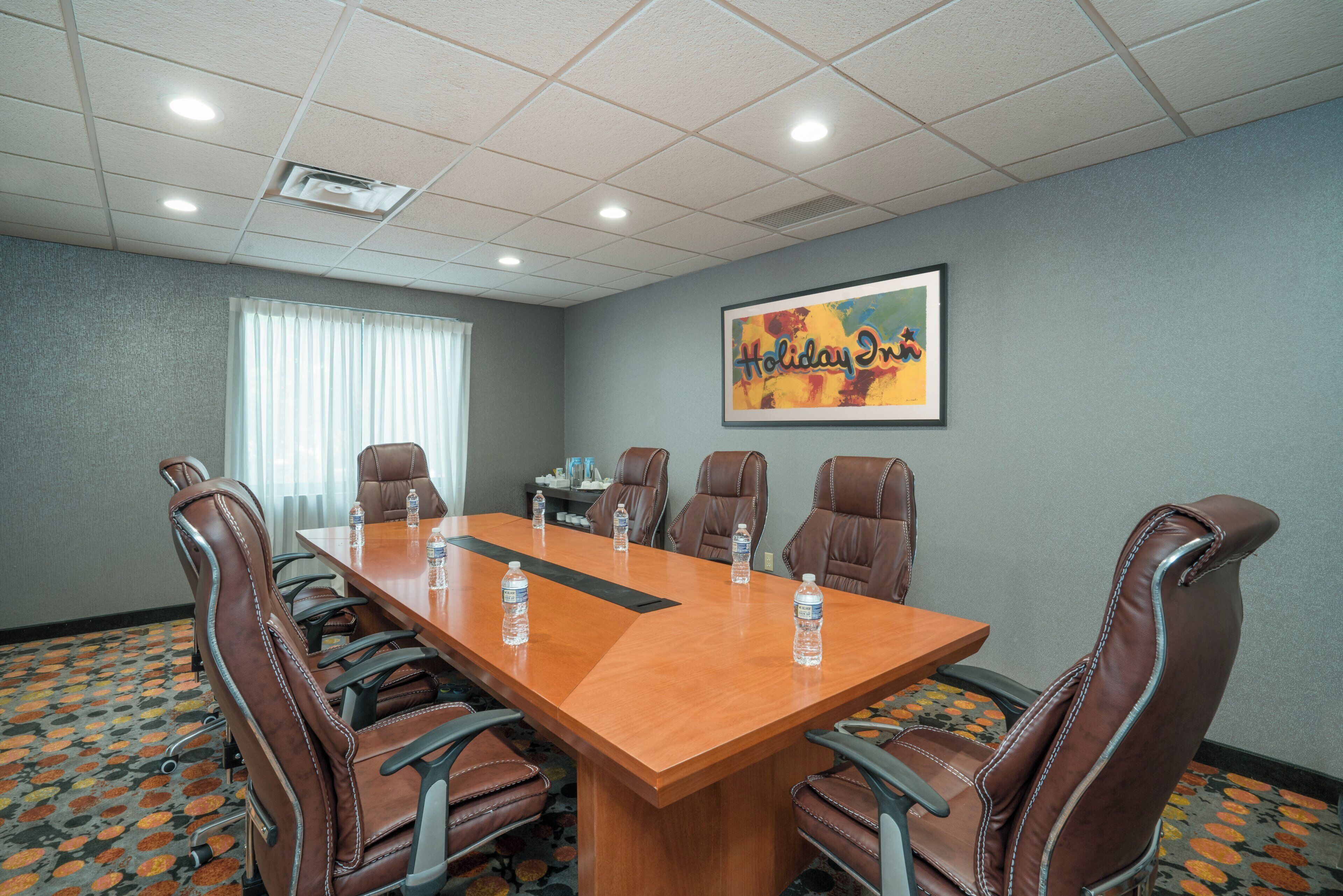 A conference room with a long table, six leather chairs, and a 'Holiday Inn' sign on the wall.