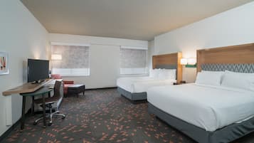 Habitación de hotel con dos camas, un escritorio con silla, televisor y alfombra con diseño geométrico.