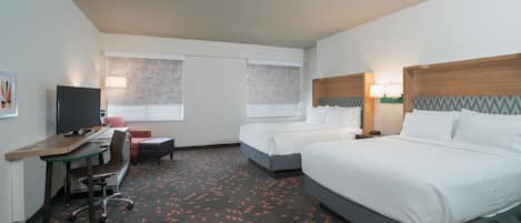 Habitación de hotel con dos camas, un escritorio con silla, televisor y alfombra con diseño geométrico.