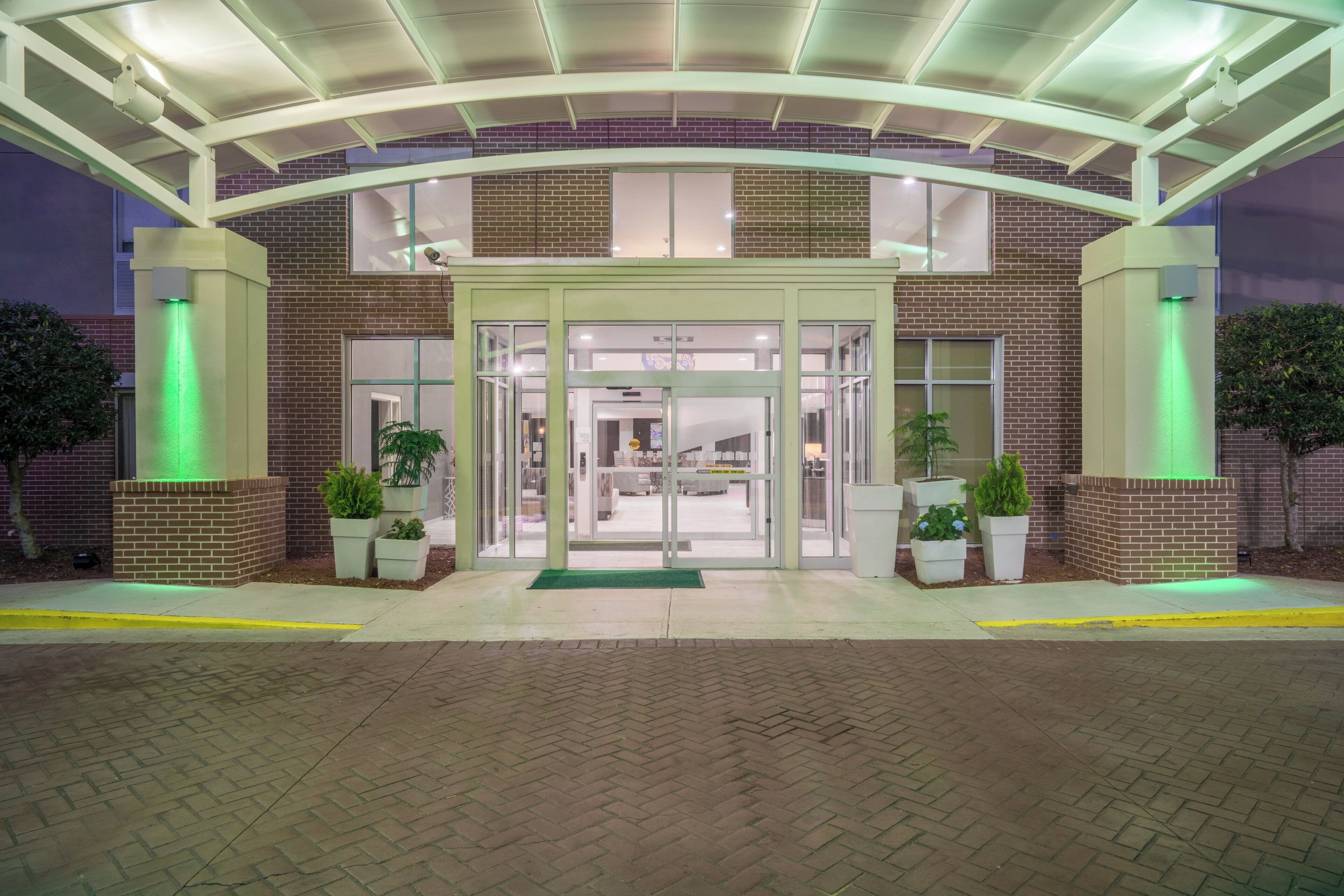 A brick building with a glass entrance, green lighting, and potted plants.