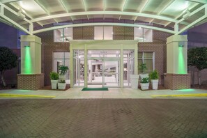 A brick building with a glass entrance, green lighting, and potted plants. - Holiday Inn Atlanta/Roswell by IHG (Roswell)