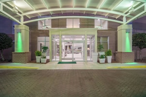 Un edificio de ladrillo con entrada de vidrio, iluminación verde y plantas en macetas.