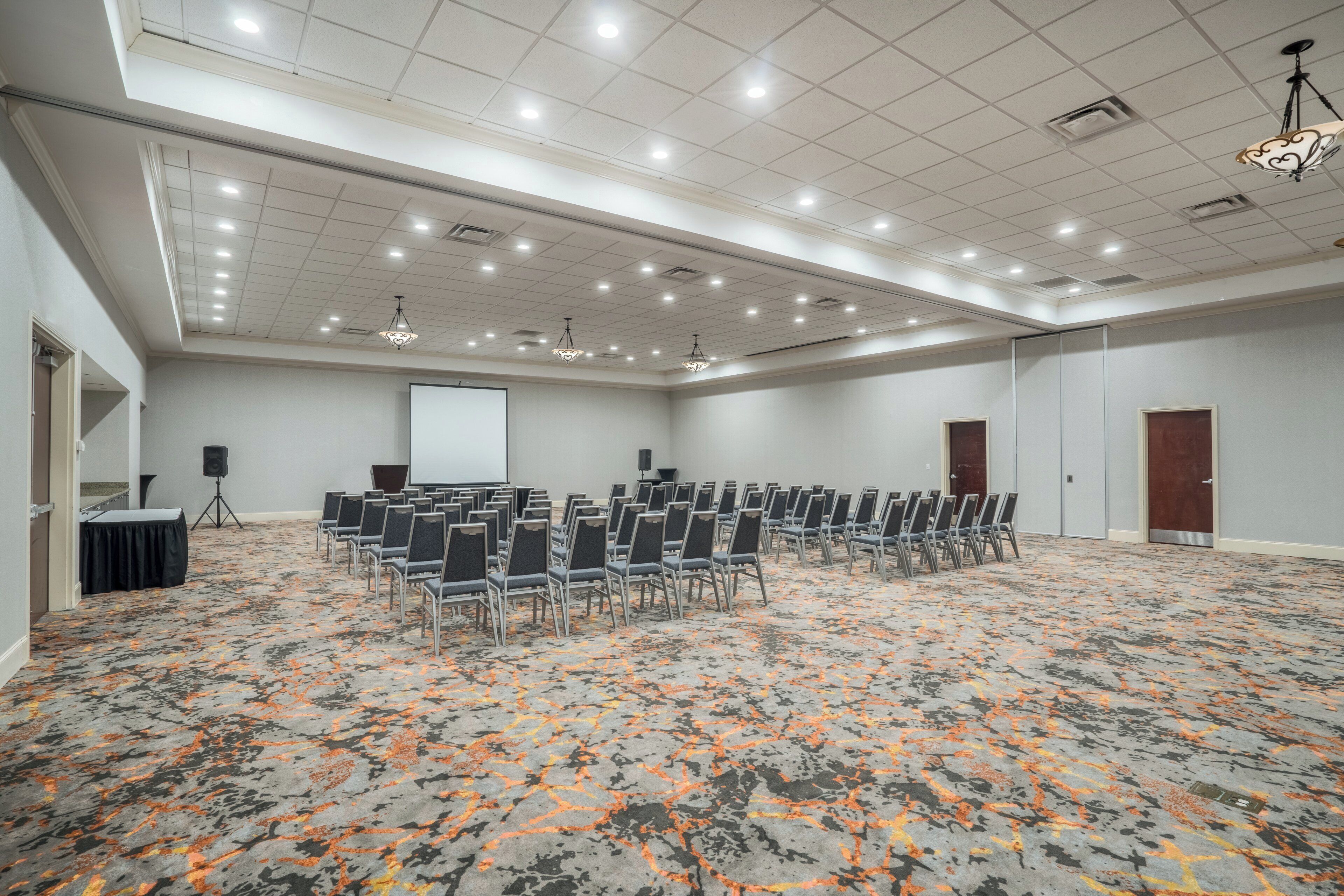 A conference room with rows of chairs, a projector screen, and a speaker on a stand.