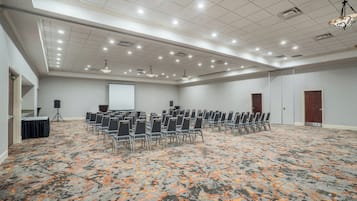 A conference room with rows of chairs, a projector screen, and a speaker on a stand.