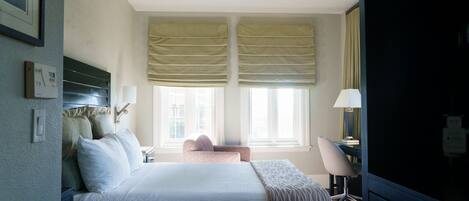 A hotel room with a bed, bedside table, lamp, and a view of the city through large windows.