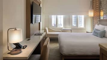 Ein Hotelzimmer mit Bett, Schreibtisch mit Lampe, Stuhl, kleinem Tisch und Fernseher.
