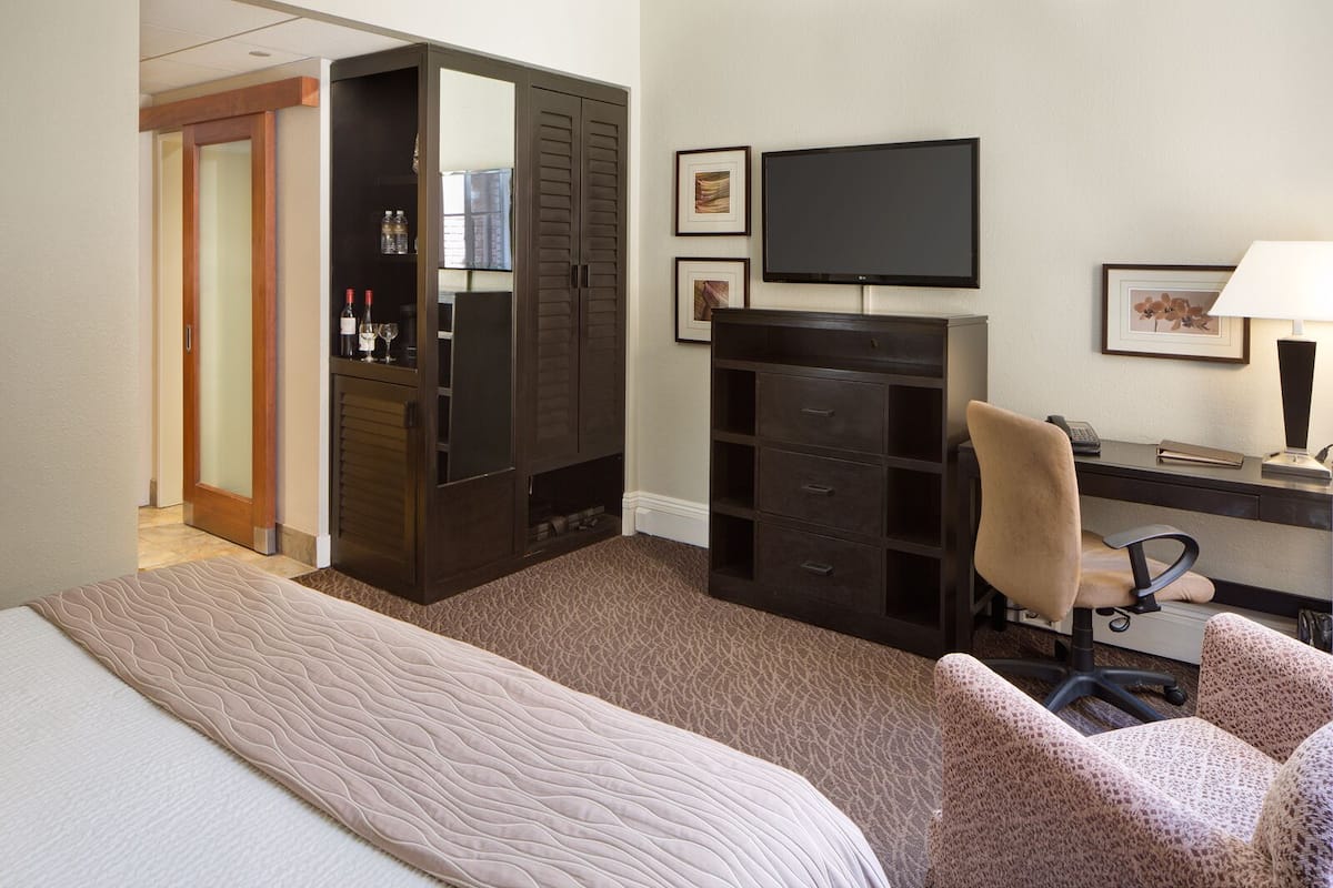 A hotel room with a bed, a desk with a chair, a TV, a wardrobe, and a mirror.