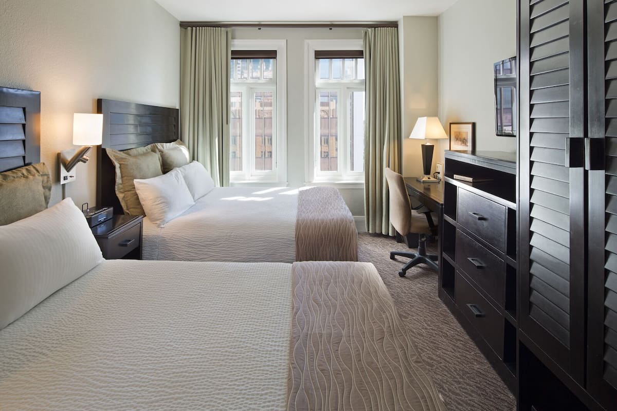 A hotel room with two beds, a desk, a chair, and a dresser.