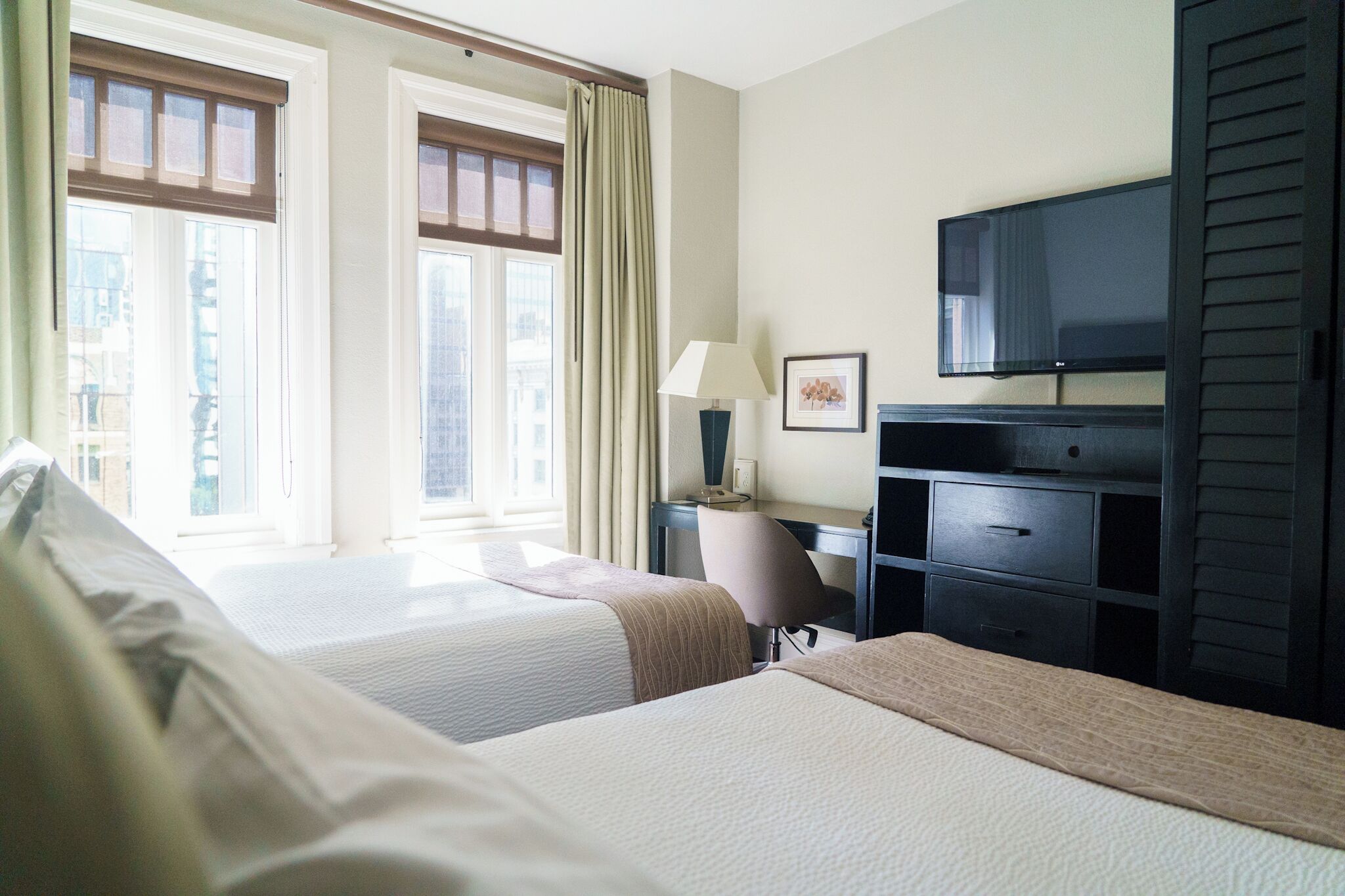 A hotel room with two beds, a desk, a chair, a TV, and a window with curtains.
