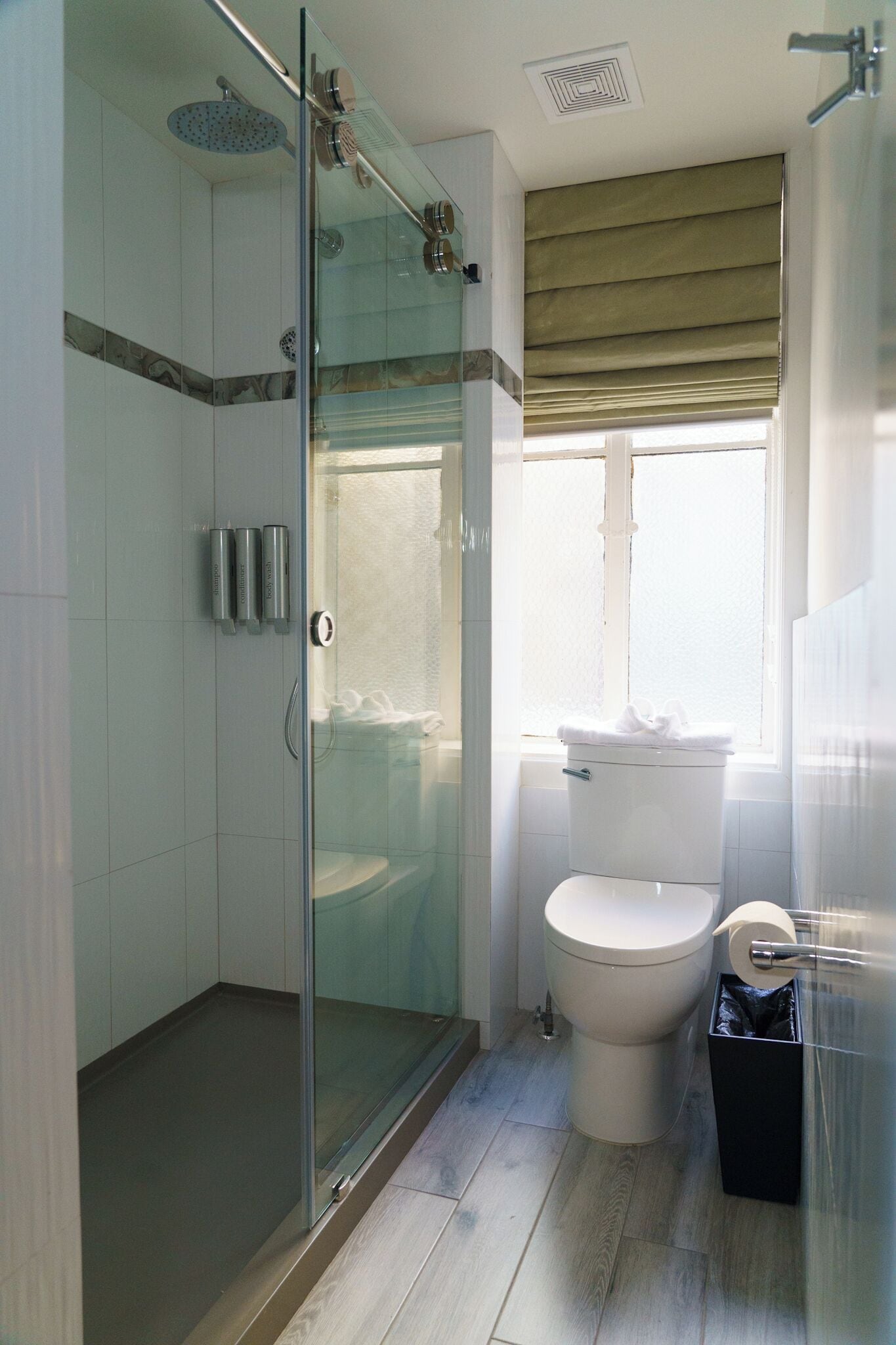 A modern bathroom with a glass-enclosed shower, a toilet, and a window with a blind.