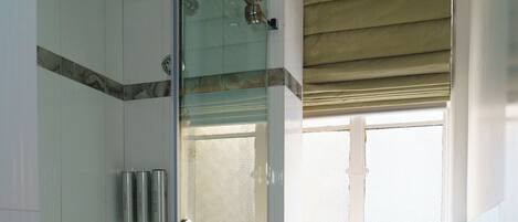A modern bathroom with a glass-enclosed shower, a toilet, and a window with a blind.