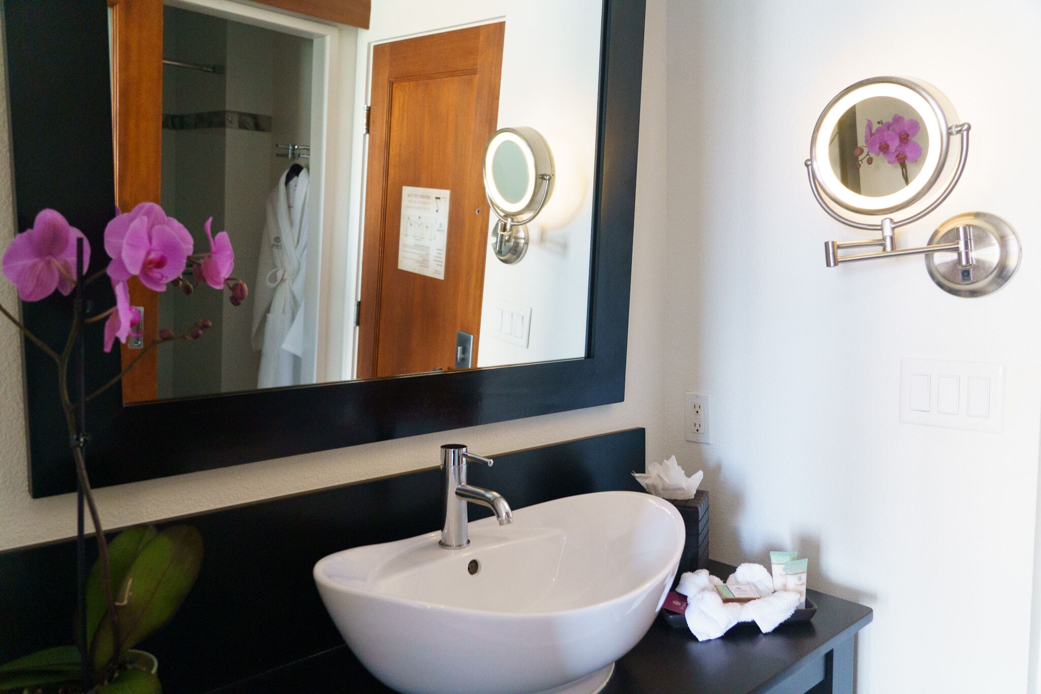 A bathroom with a white sink, a large mirror, and a small round mirror on the wall.
