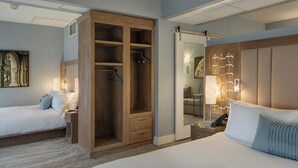 Habitación de hotel con un amplio vestidor, cama con ropa de cama blanca, mesita de noche con lámpara y un espejo adosado a la pared.