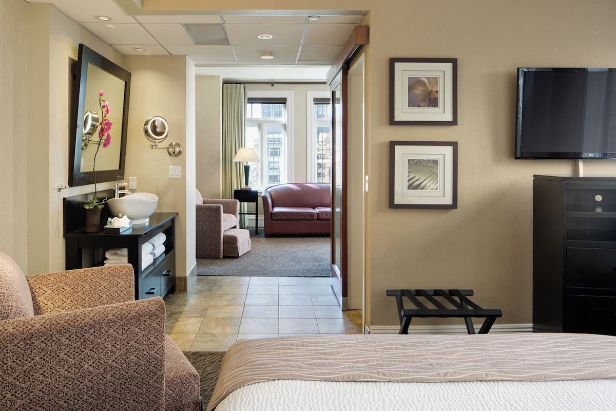 A hotel room with a bed, a desk with a mirror, a sink, a sofa, and a television.