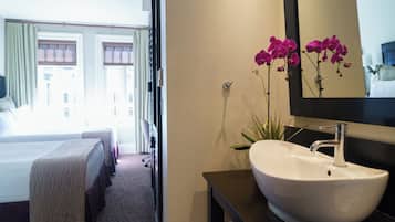 A hotel room with a bed, a bedside table with a white sink, and a mirror.