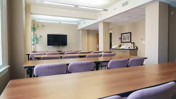 A conference room with long tables and chairs, a flat-screen TV, and a plant.