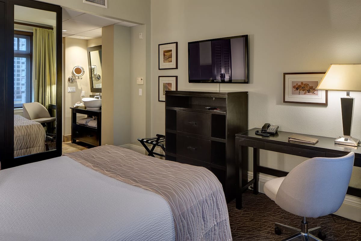 A hotel room with a bed, a desk, a chair, a TV, and a mirror.