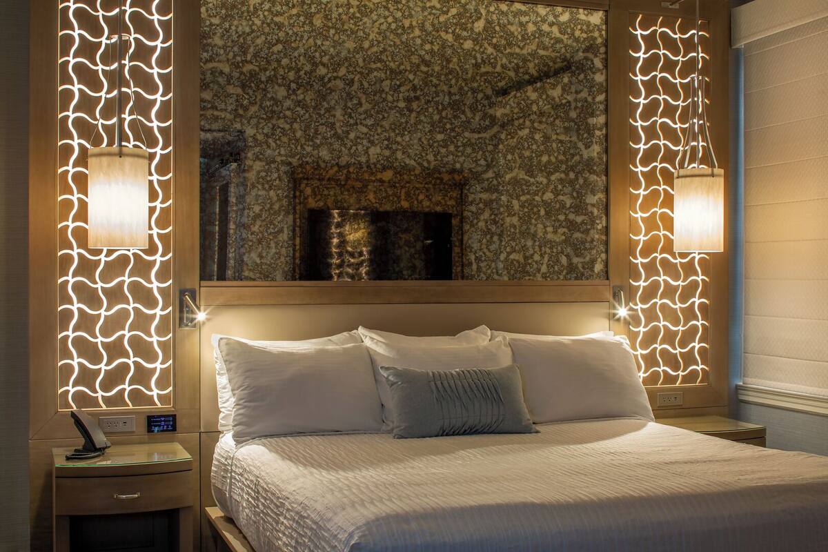 A neatly made bed with white linens and a gray throw pillow, flanked by two bedside tables with lamps.