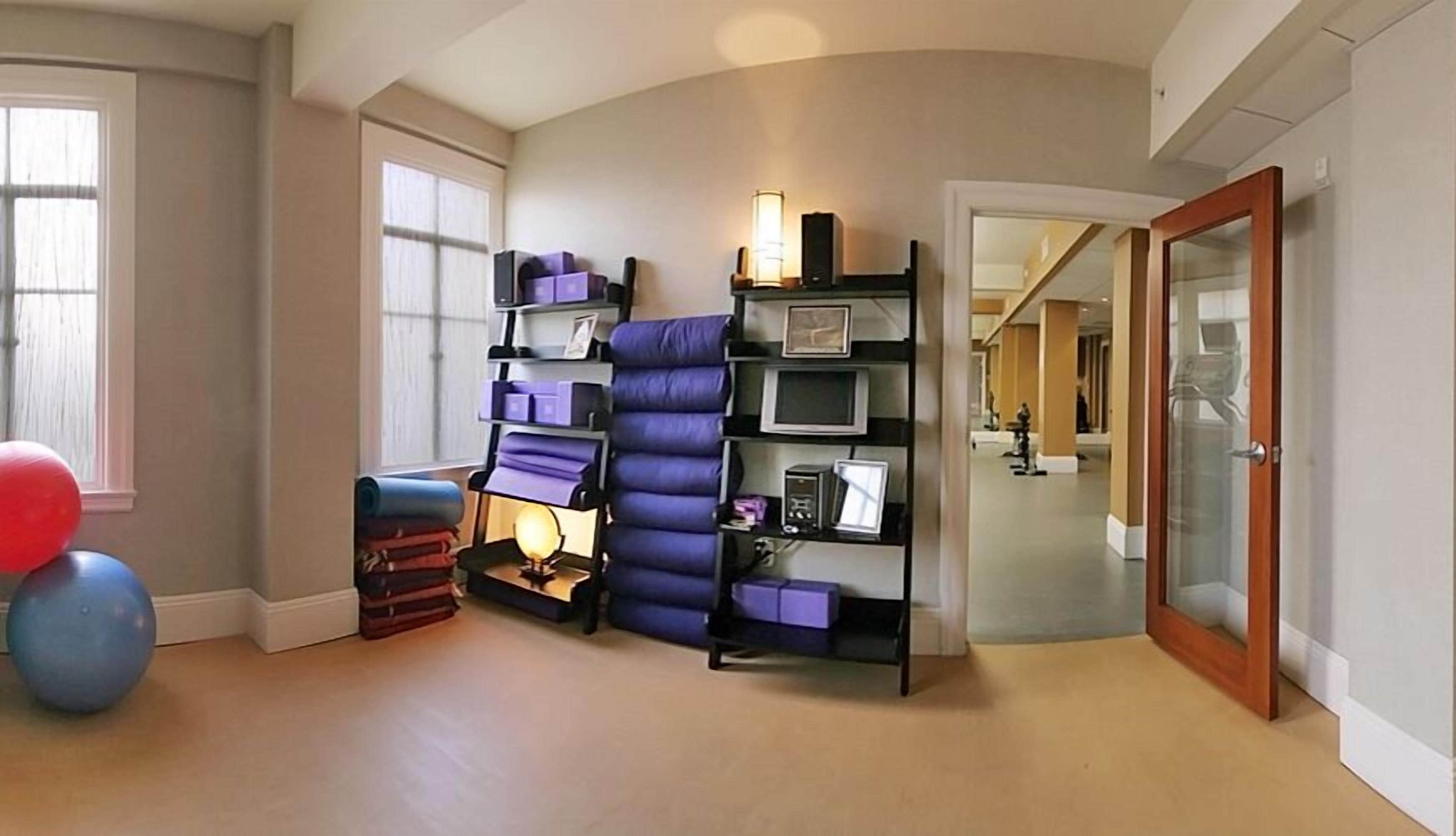 Ein Zimmer mit gewölbter Decke, einem großen Fenster, einem blauen Fitnessball, einer Yogamatte und einem Bücherregal mit violetten Aufbewahrungsboxen.