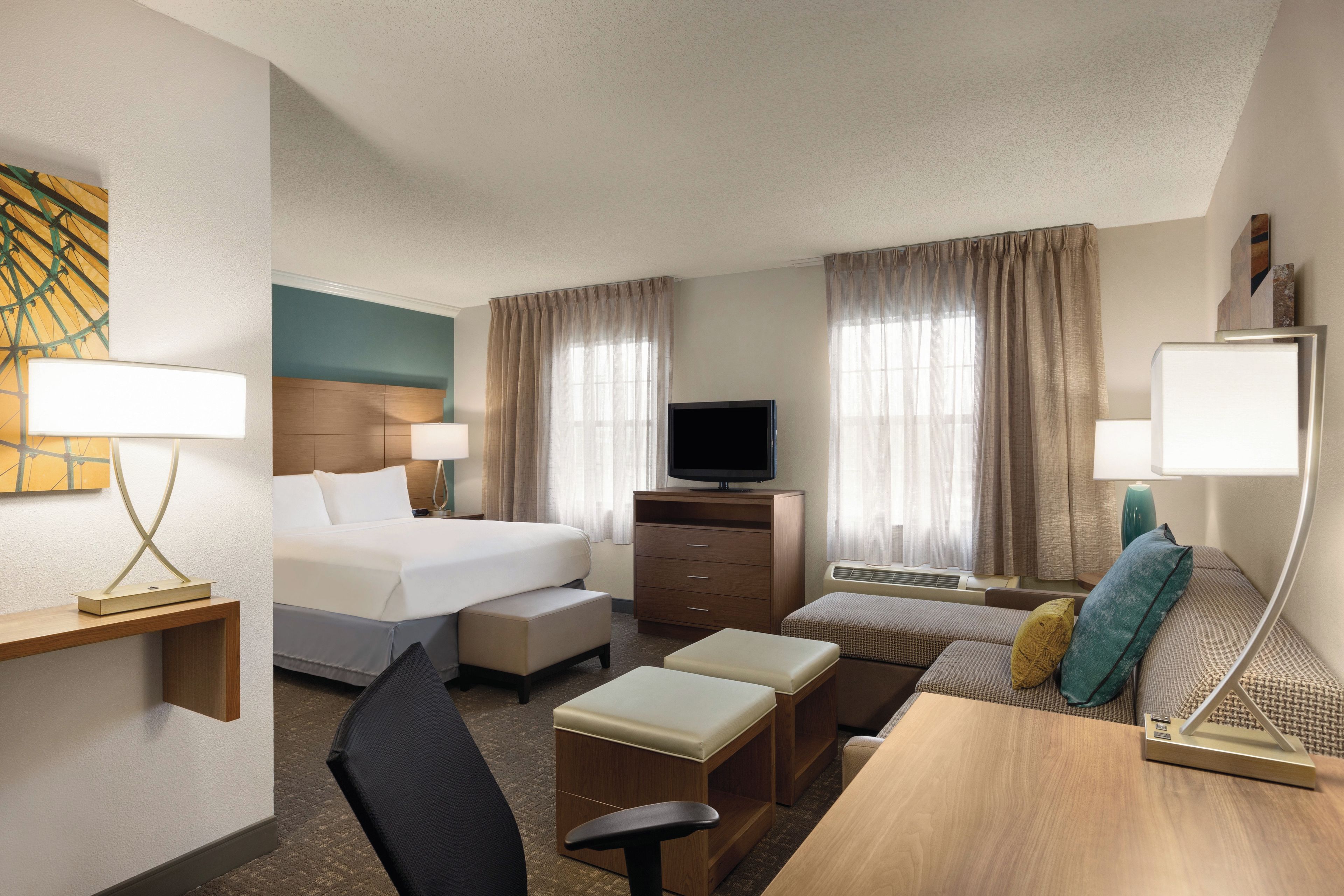A hotel room with a bed, a desk, a chair, a TV, and a sofa.
