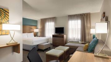 A hotel room with a bed, a desk, a chair, a TV, and a sofa.