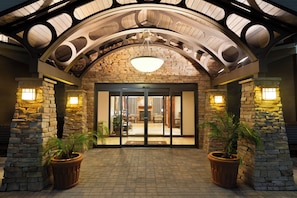 A hotel entrance with a stone facade, a glass door entrance, and two potted plants.